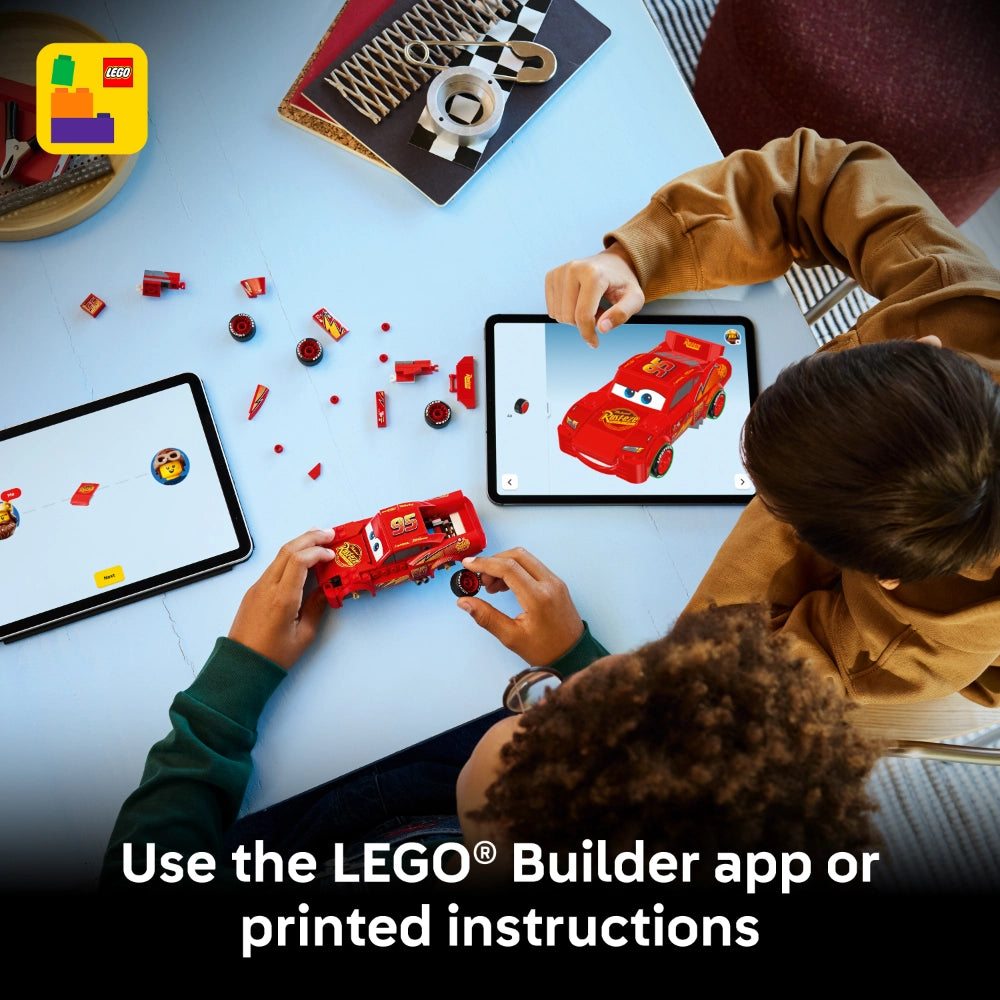 Child building red LEGO Lightning McQueen car from Disney Pixar Cars with LEGO bricks, viewing instructions on tablet and holding assembled model, with LEGO Builder app logo and scattered red pieces on blue surface