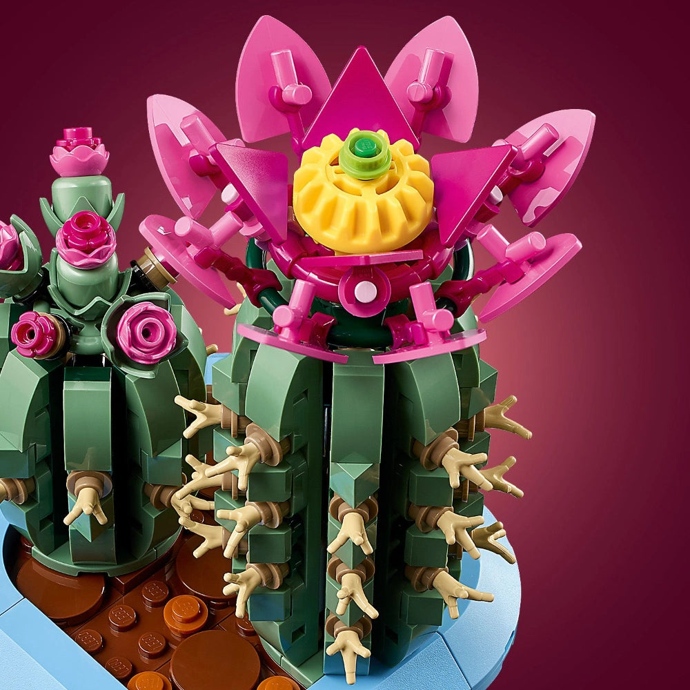 LEGO Flowering Cactus set 10309 featuring buildable cacti with pink and yellow blooms, green segmented stems, tan spines, displayed against a magenta background with brown terracotta pot base and blue platform