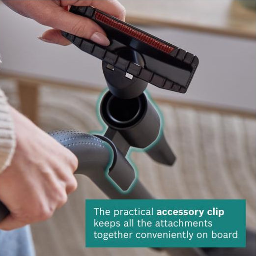 Person holding a vacuum cleaner with an accessory clip attached, featuring text about the clip's functionality.