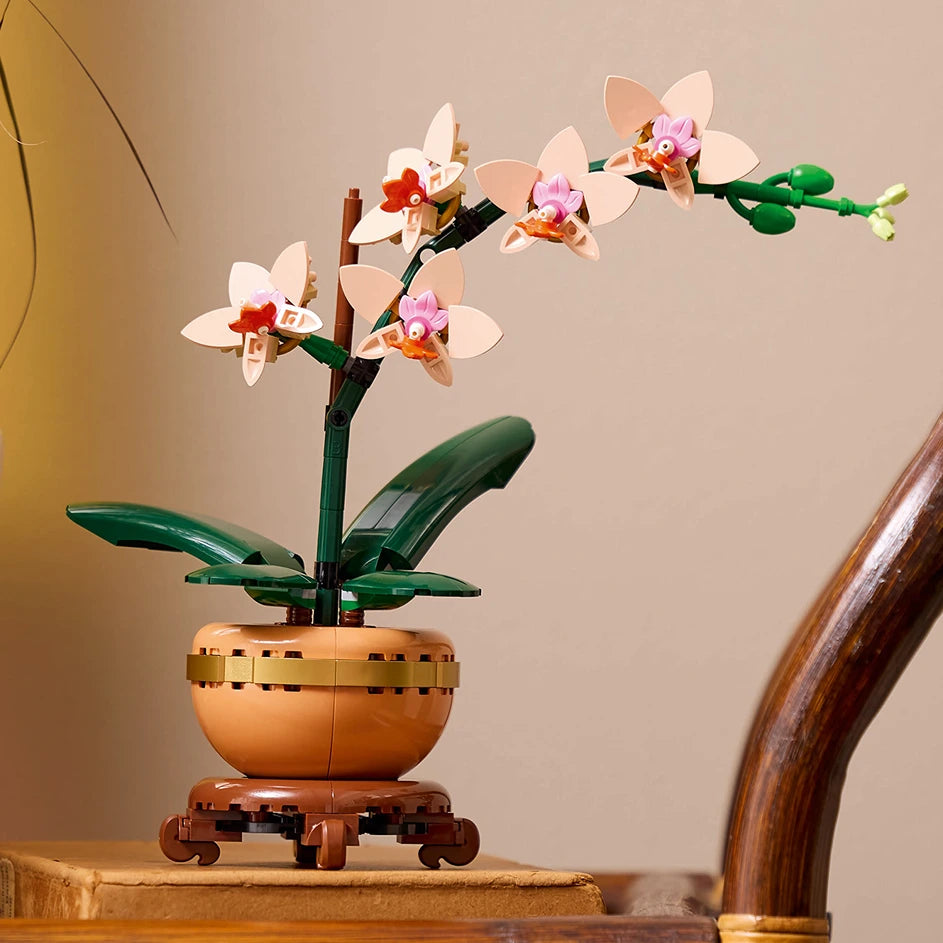 LEGO Mini Orchid 10343 set displaying constructed white and pink orchid flowers with orange centers in a tan and brown decorative pot with green leaves on a wooden surface