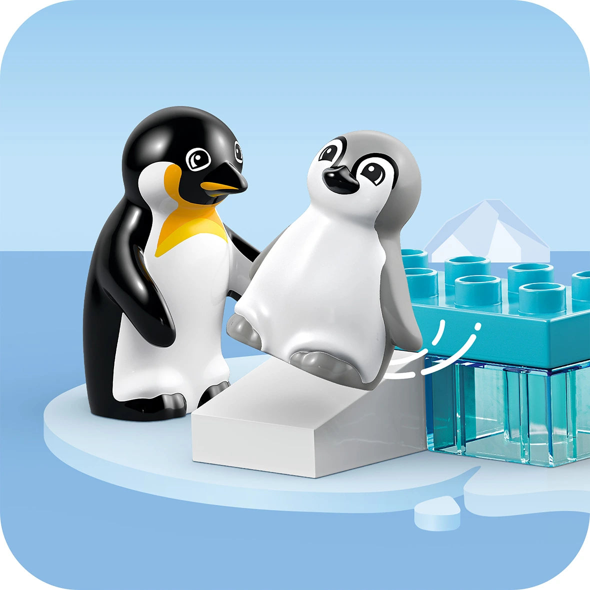 Two LEGO penguins in black, white and gray plastic on an icy blue platform surrounded by transparent blue LEGO ice blocks and crystalline structures against a clear blue sky and water background