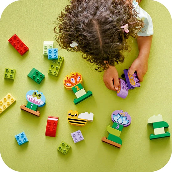 Child playing with colorful LEGO bricks on yellow background, building garden and flower themed creations including a bee, flower, and butterfly figures in red, green, blue and purple