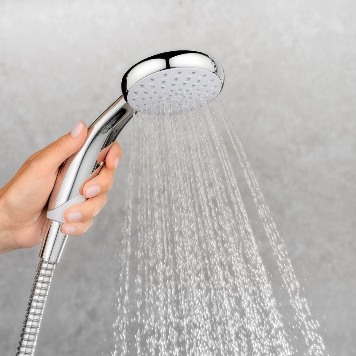 Hand holding a shower head with water spraying against a gray background