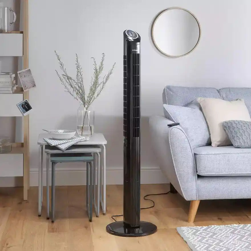Black Dimplex Mont Blanc tower fan in modern living room setting with grey sofa, nesting tables, dried flowers in vase, round mirror and wooden flooring