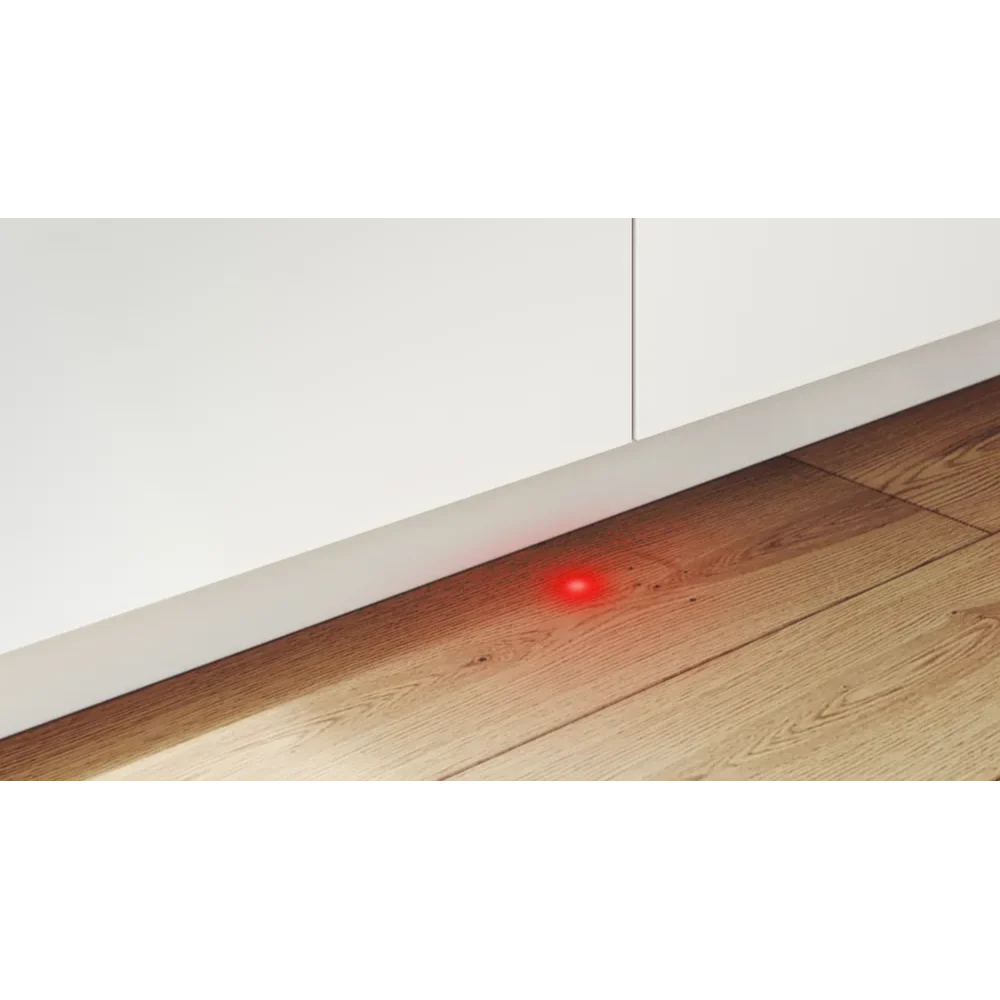 Close-up of white integrated dishwasher with red indicator light on wooden flooring against white baseboard and wall