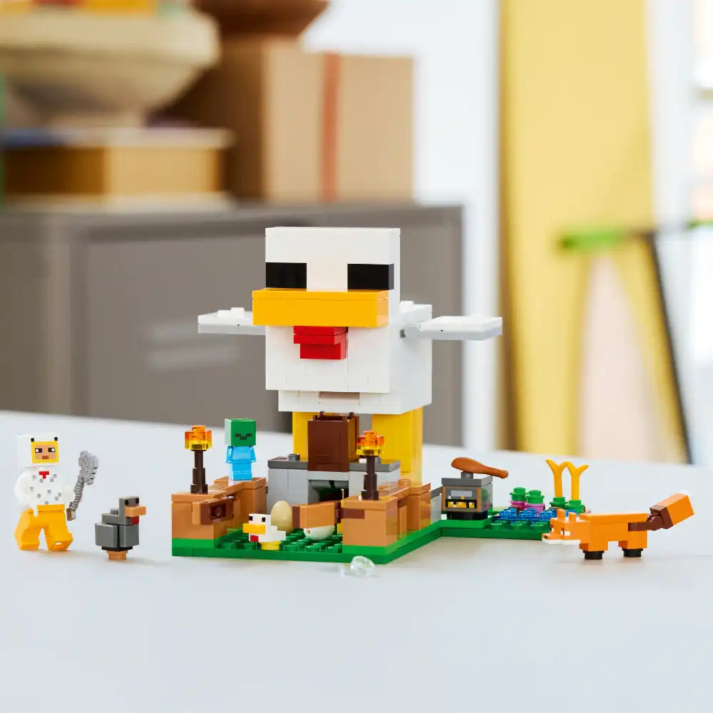 LEGO Minecraft Chicken Farm set 21585 featuring a large white and yellow pixelated chicken minifigure with outstretched arms, surrounded by small character minifigures including a farmer and animals on a green baseplate with brown wooden farm structures and accessories displayed on white surface