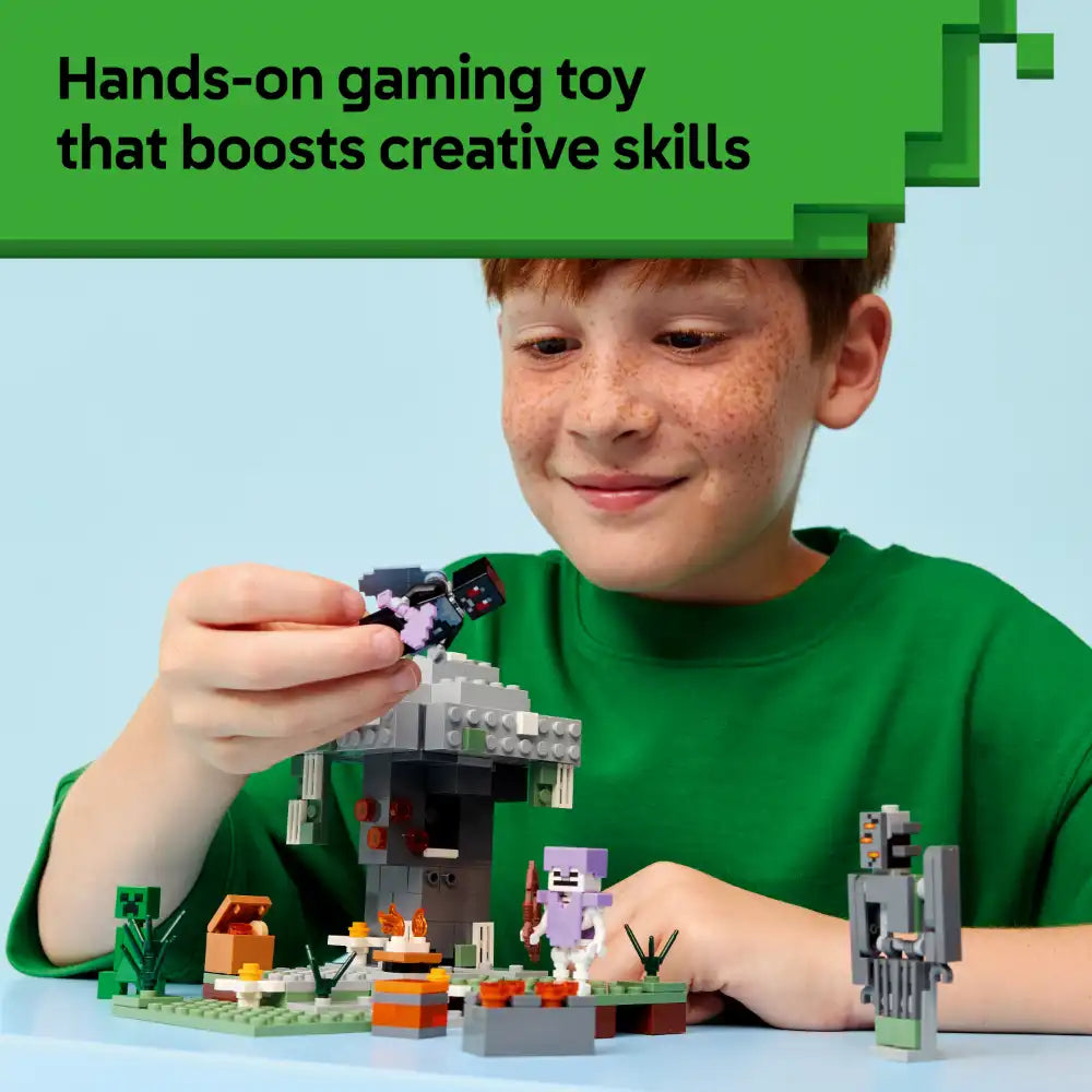 Young boy in green shirt playing with LEGO Minecraft The Pale Garden set, holding a purple character figure above a constructed scene featuring gray stone tower, green base plate, orange and brown blocks, and various Minecraft-themed pieces against light blue background