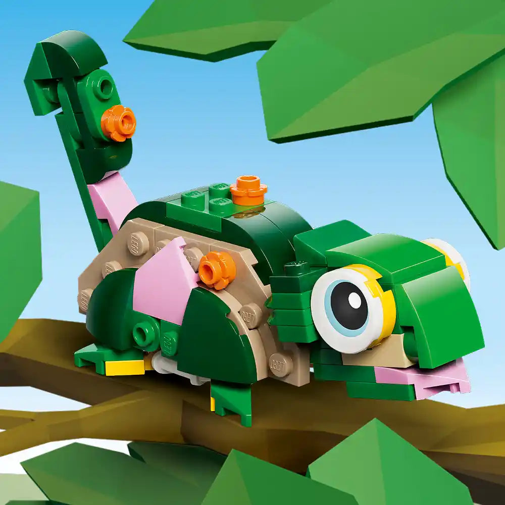 LEGO Creator turtle building set 31377 featuring a green brick turtle with orange details, pink accents, and a large yellow-rimmed eye, perched on a brown branch with green foliage against a blue sky background