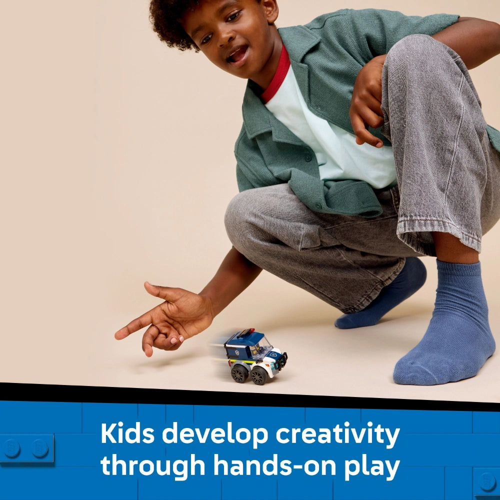Young child in green cardigan and blue socks crouching down to play with a small blue and white LEGO police truck toy on a beige surface, demonstrating hands-on creative play