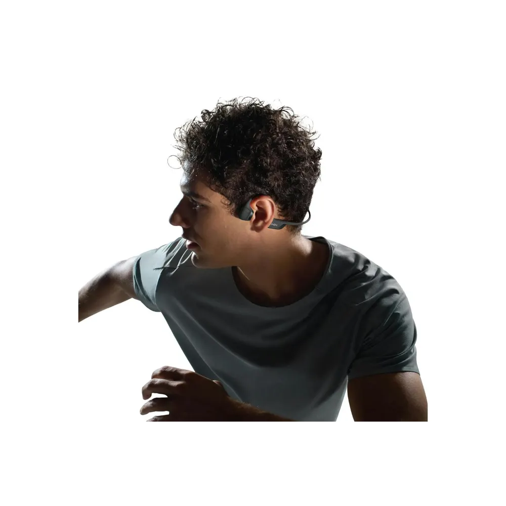 Man wearing grey t-shirt demonstrating black Shokz OpenRun Pro 2 Mini open ear wireless headphones with bone conduction technology, shown in profile view against white background