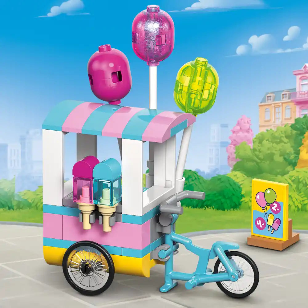 LEGO Friends ice cream and balloon stand set 42692 featuring a colorful pastel pink, turquoise and yellow mobile cart with striped awning, three hanging balloon accessories in pink and lime green, ice cream cones, a blue bicycle, and an instruction card on a bright outdoor background