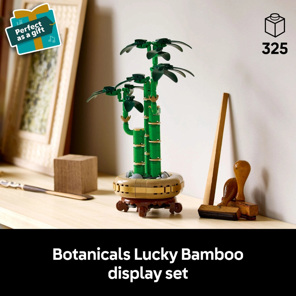 LEGO Botanicals Lucky Bamboo display set featuring green buildable bamboo stalks with leaves in a tan and brown decorative pot, accompanied by wooden plant care accessories, displayed on a shelf with "perfect as a gift" badge and 325 piece count indicator