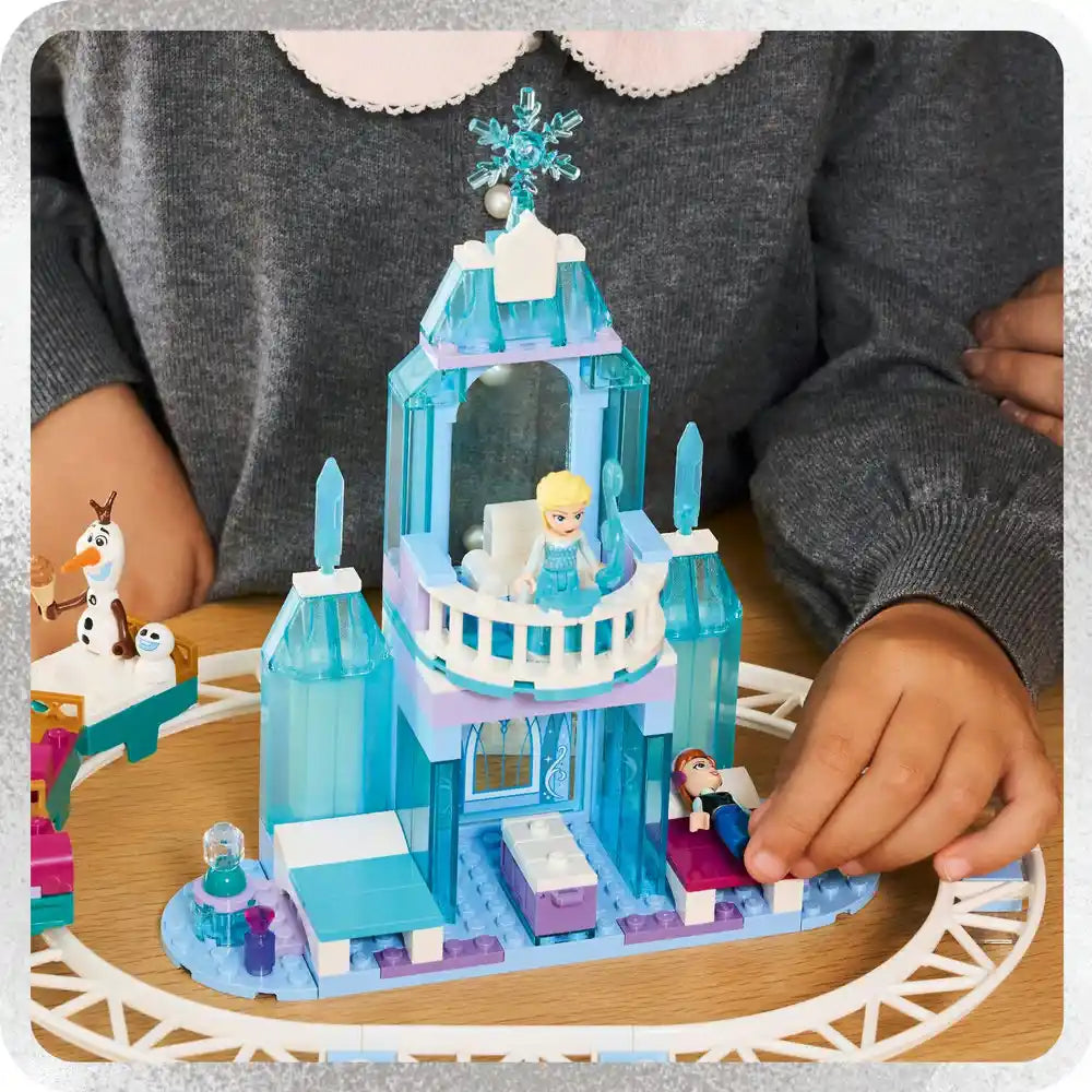 Child playing with LEGO Elsa's Ice Castle set featuring turquoise and white castle tower with snowflake topper, Elsa minifigure, Olaf snowman character, and circular track base on wooden floor