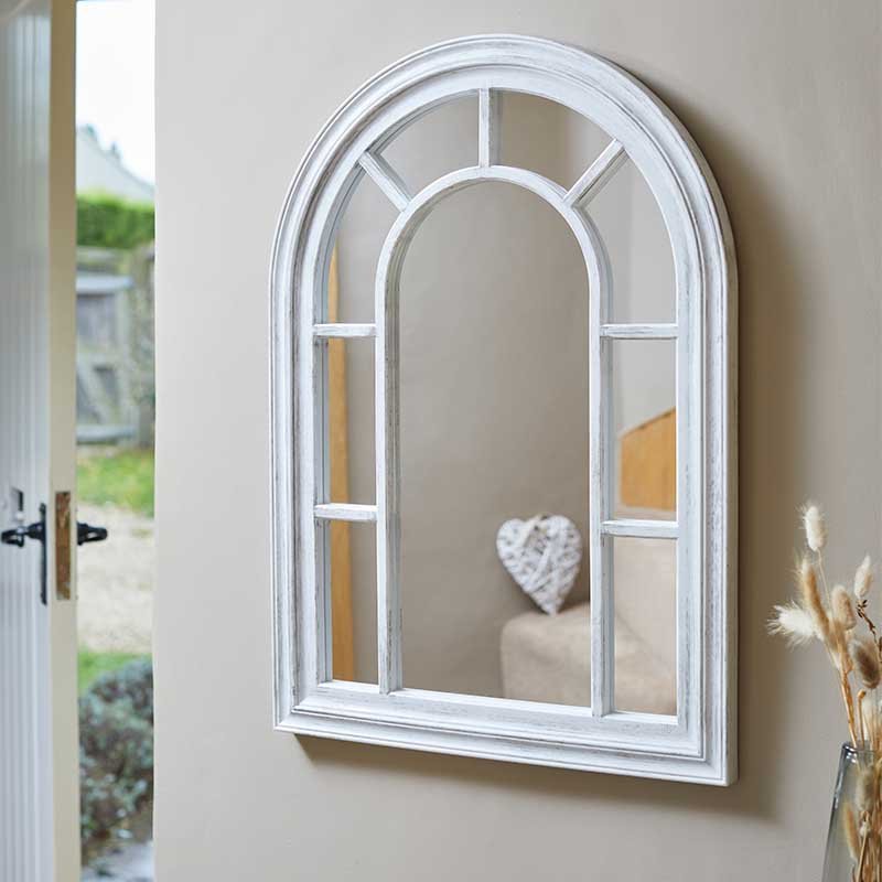 Silvergris arched window-style wall mirror with white frame and geometric pane divisions, displayed in a bright interior setting near open garden doors with dried pampas grass decoration