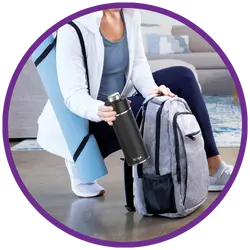 Person packing a backpack with a yoga mat and water bottle in a home setting.