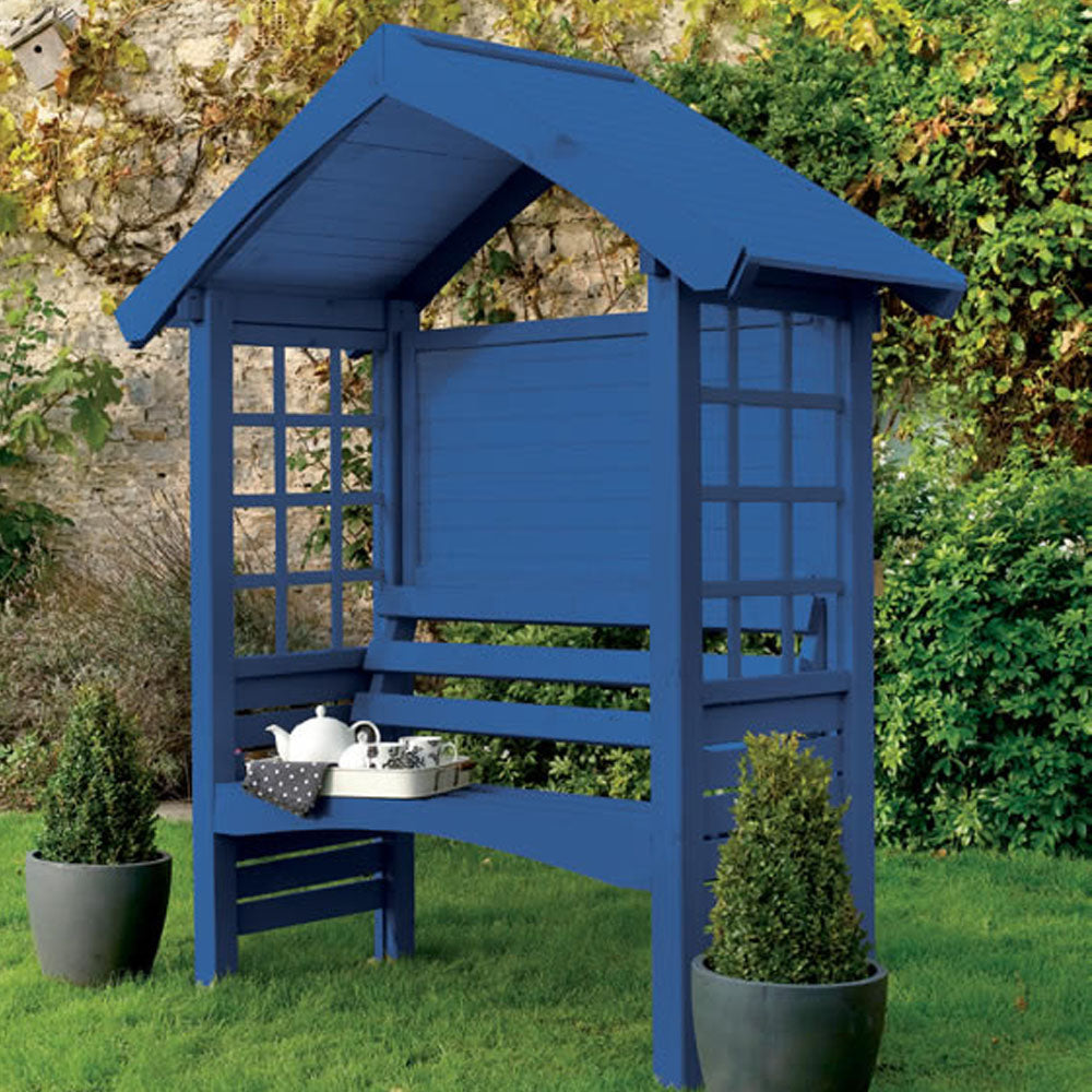 Blue wooden garden arbor with bench seating and latticed windows in a garden setting with ivy and potted plants