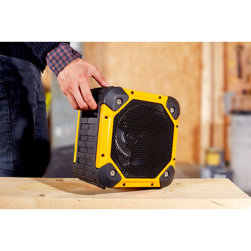 Man in checkered shirt holding yellow and black Dimplex Rugged Workshop Electric Fan Heater 3KW on wooden table in construction site setting