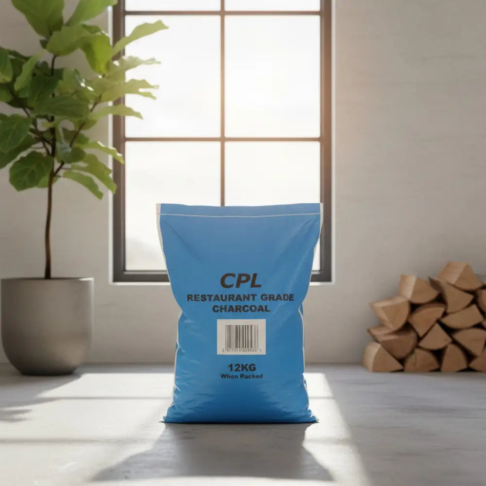 Blue CPL Restaurant Grade Charcoal 12kg bag displayed on a light gray surface near a potted green plant, windows, and stacked firewood in a minimalist interior setting