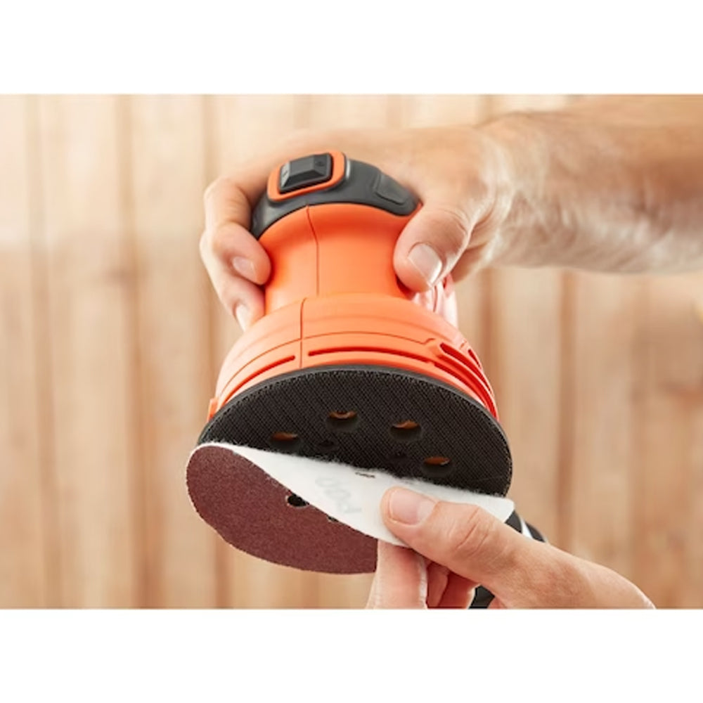 Black & Decker BEW210 random orbital sander with orange and black body held in hands showing removable sanding pad against wooden background