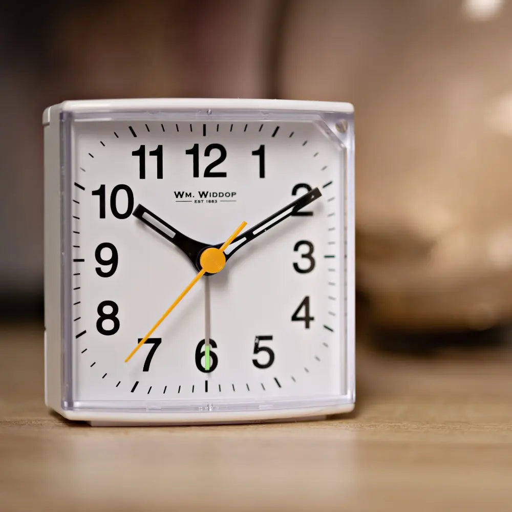 White square alarm clock by Wm. Widdop with black numerals, black hour and minute hands, yellow second hand, yellow center circle, and sweep movement mechanism on wooden surface