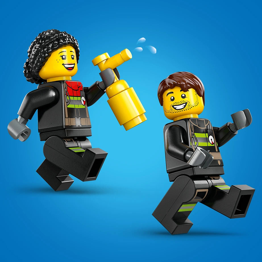 Two smiling LEGO minifigures in black and yellow firefighter uniforms with reflective stripes celebrate against a bright blue background, one holding a yellow fire hose nozzle