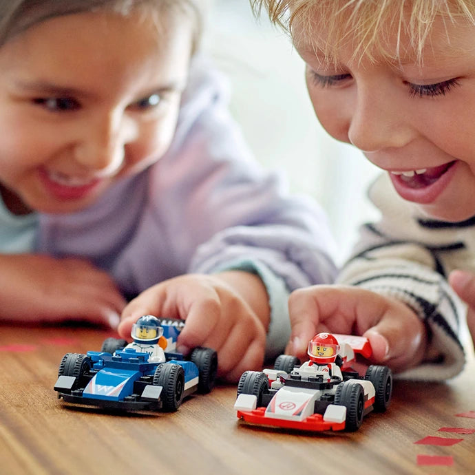 Two young children playing with LEGO F1 racing cars on a wooden surface, featuring a blue Williams F1 car and a red and white Haas F1 car with minifigures, demonstrating interactive play