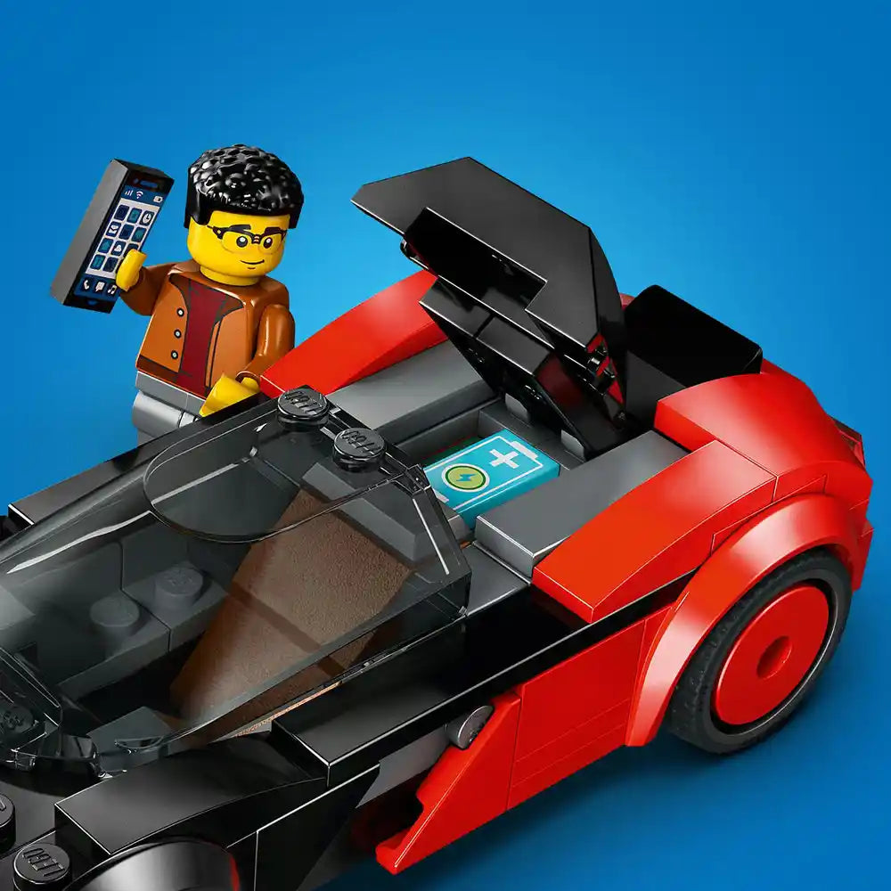 LEGO EV Supercar set 60486 featuring a red and black electric sports car with opening doors, a yellow minifigure with black hair wearing orange and red jacket holding a mobile phone, black steering wheel, blue instruction manual, and gray interior details against a bright blue background