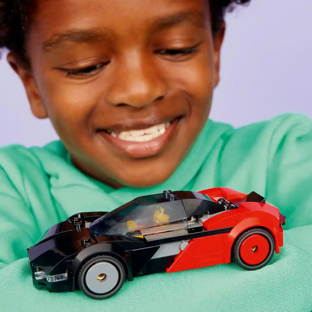 Child in green shirt smiling at LEGO 60486 EV Supercar set featuring red and black buildable sports car model on mint green surface