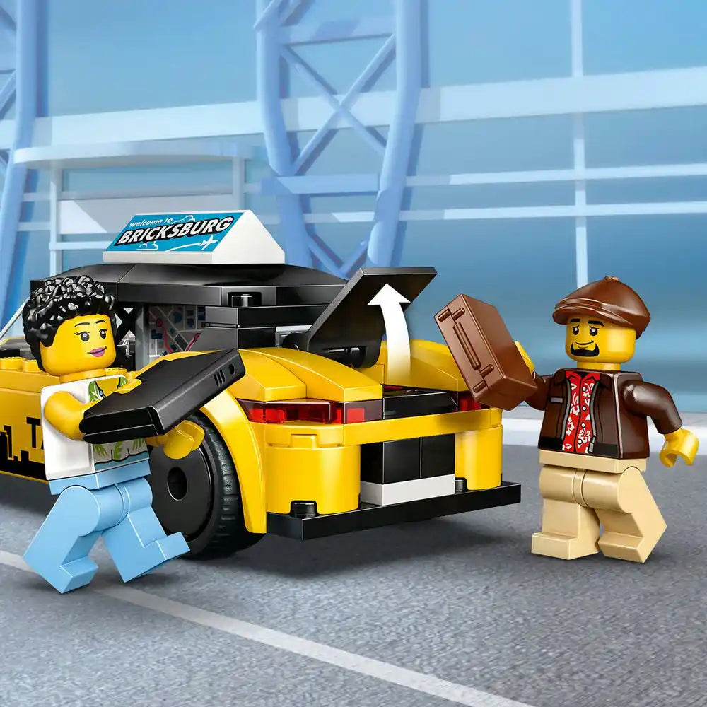 LEGO yellow taxi set 60487 featuring bright yellow brick-built taxi car with black and white details, two minifigures including driver with black hair and passenger in brown jacket and cap, displayed against modern blue building backdrop with Bricksburg sign