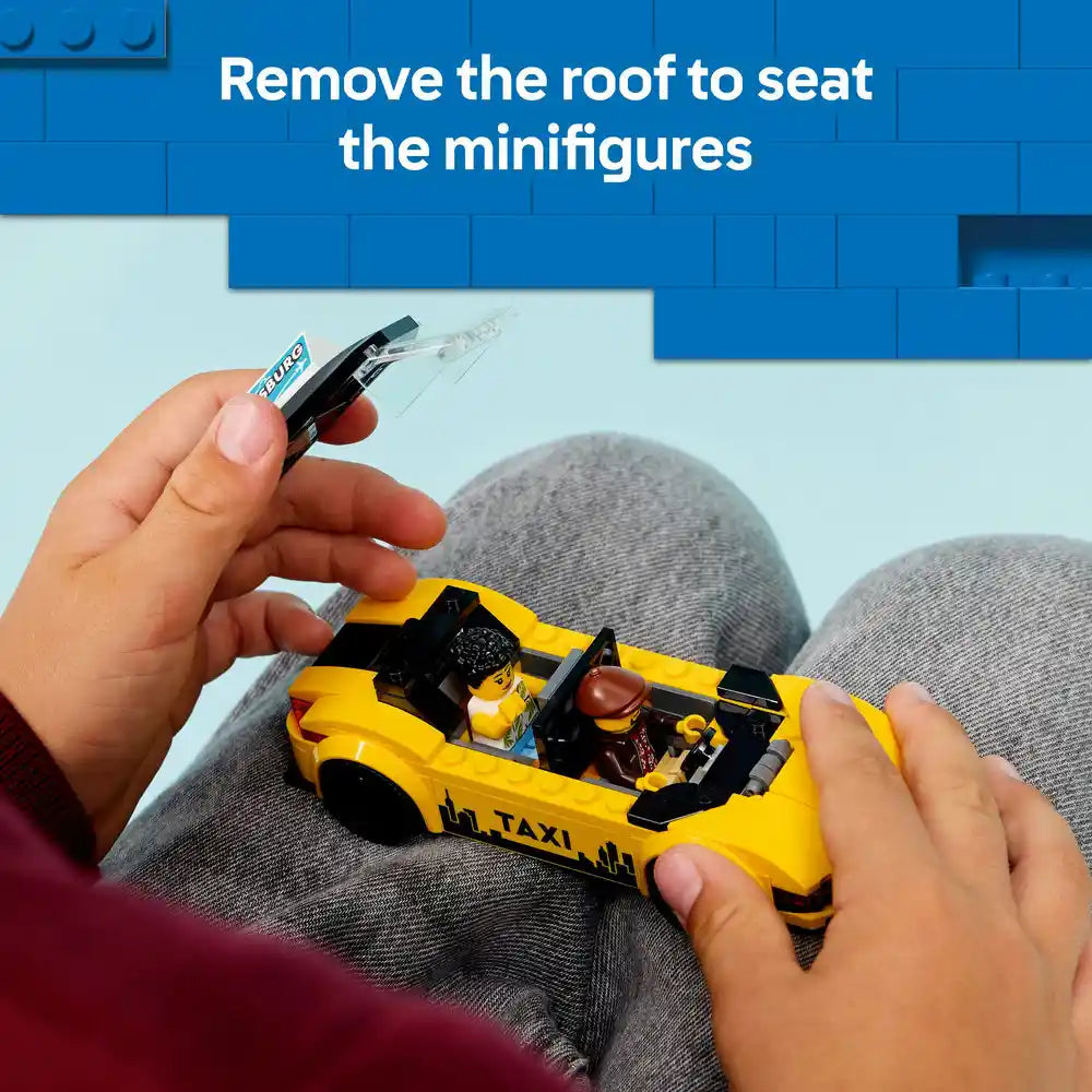 Child's hands holding a bright yellow LEGO taxi car with black details and minifigures visible inside, demonstrating how to remove the removable roof piece to access the seated minifigures, against a blue LEGO brick background