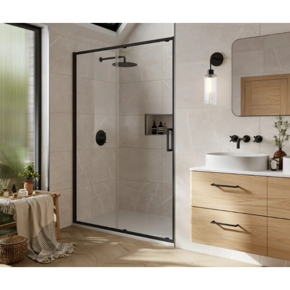 Modern bathroom featuring a Merlyn 6 Series black framed sliding shower door with frosted glass panels, chrome fixtures and rainfall showerhead, light wood vanity with white countertop and vessel sink, wall-mounted black faucet, pendant lighting, beige tile walls and flooring, green window with plants, and contemporary Scandinavian styling