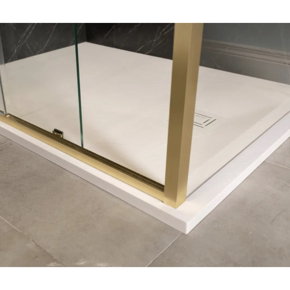 Modern Merlyn 6 Series sleek sliding shower door with brushed brass frame and clear glass panel installed in white acrylic shower tray with dark marble-effect wall panels in contemporary bathroom setting