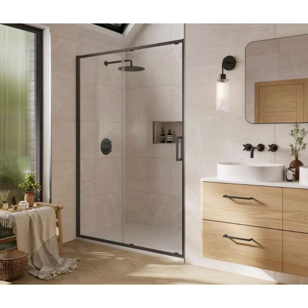Modern bathroom featuring Merlyn 6 Series Sleek sliding shower door with black frame and frosted glass panel, light wood vanity with white countertop, black wall-mounted faucet, pendant light, rounded mirror, beige tile walls, and natural light from window with green plants