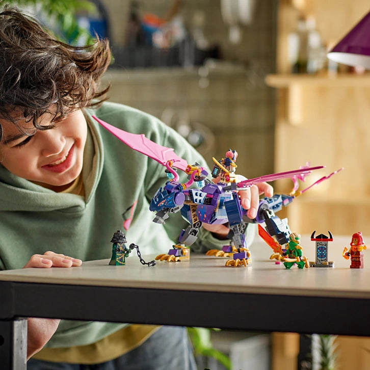 Child in green hoodie playing with LEGO Ninjago Rontu the Master Dragon set 71842, featuring a large purple and blue dragon figure with pink wings, minifigures, and accessories displayed on a white table