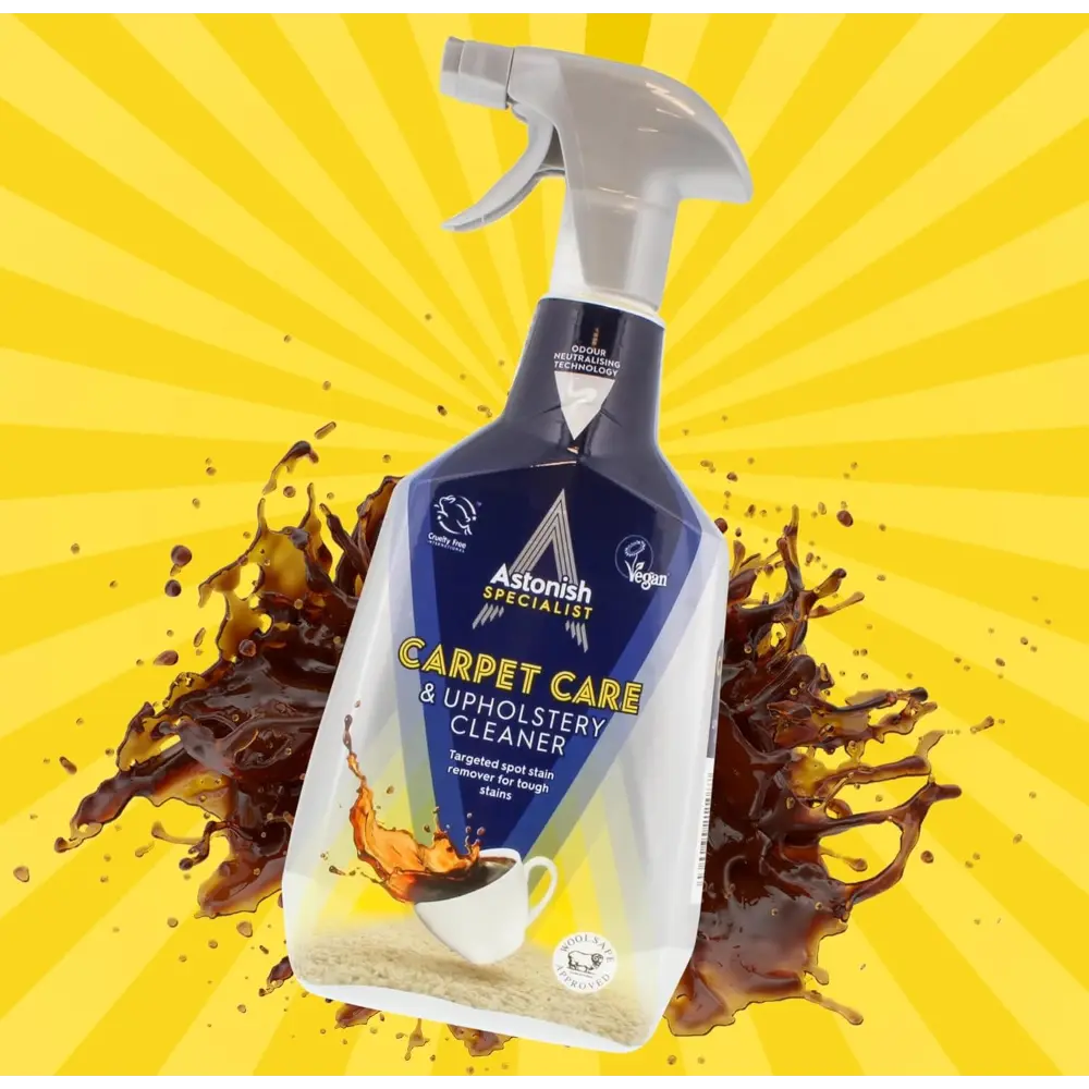 Astonish Specialist Carpet Care and Upholstery Cleaner 750ml spray bottle with trigger, featuring navy blue and white labeling, displayed against a bright yellow radiating background with brown liquid splash effects