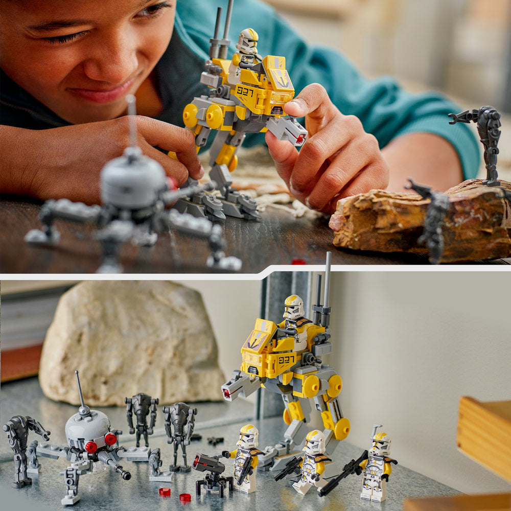 Child playing with LEGO 75431 327th Star Corps Clone Troopers Battle set featuring yellow and black buildable walker vehicle with minifigures, white and grey clone trooper soldiers, and brown rock terrain pieces displayed on grey surface