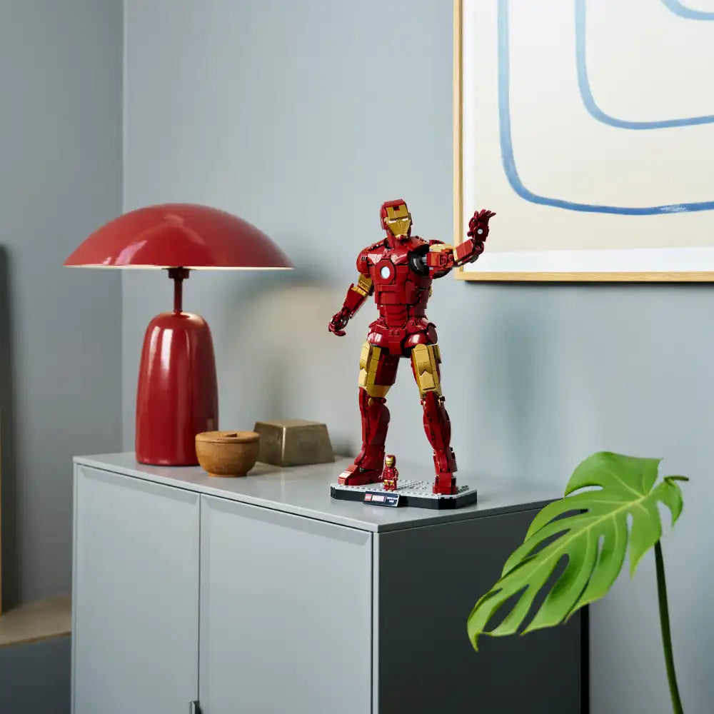 LEGO Iron Man Mark 3 Collectors Edition set 76344 displayed on white cabinet with red mushroom lamp, wooden accessories, and green Monstera plant, showcasing detailed red and gold armored minifigure in modern home decor setting