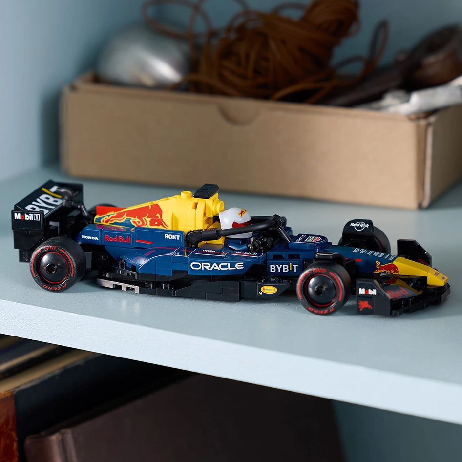 LEGO Oracle Red Bull Racing RB20 F1 race car model displayed on a light blue surface, featuring blue and yellow bodywork with black accents, sponsor logos including Oracle and Bybit, displayed in front of a cardboard storage box against a light blue wall