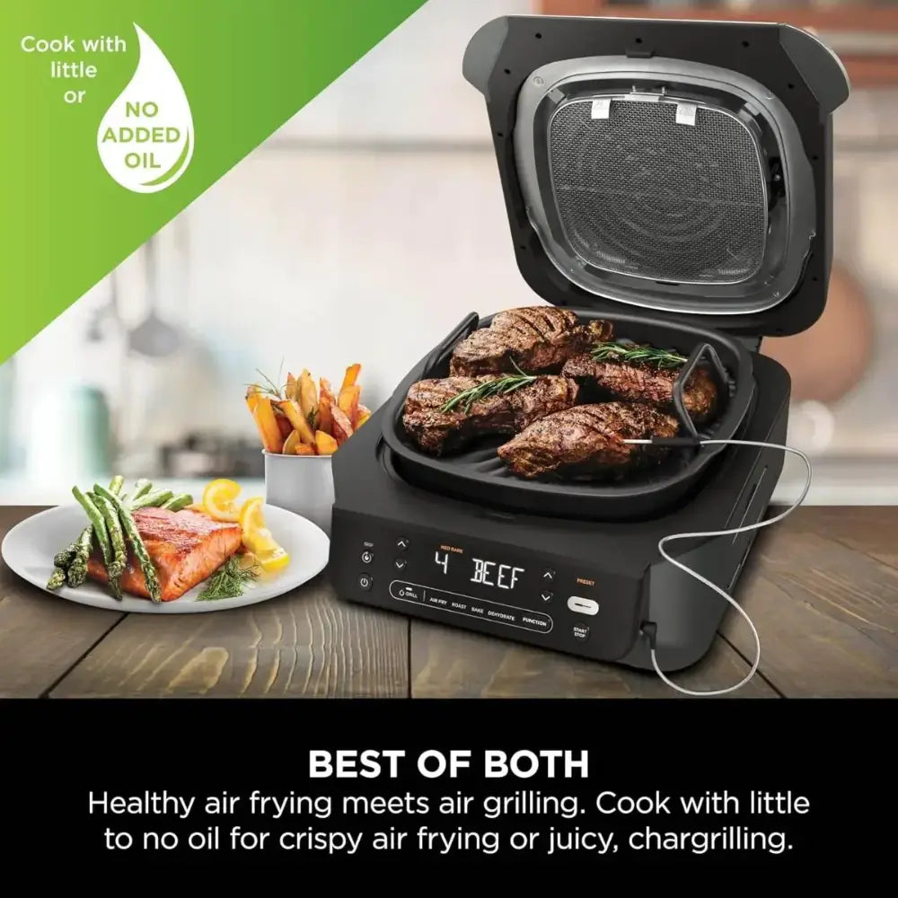 Ninja 5 in 1 black electric grill and air fryer with digital display showing beef setting, open lid revealing cooked steaks and asparagus, accompanied by plated salmon with green beans and french fries, wooden table setting with green banner highlighting no added oil cooking feature