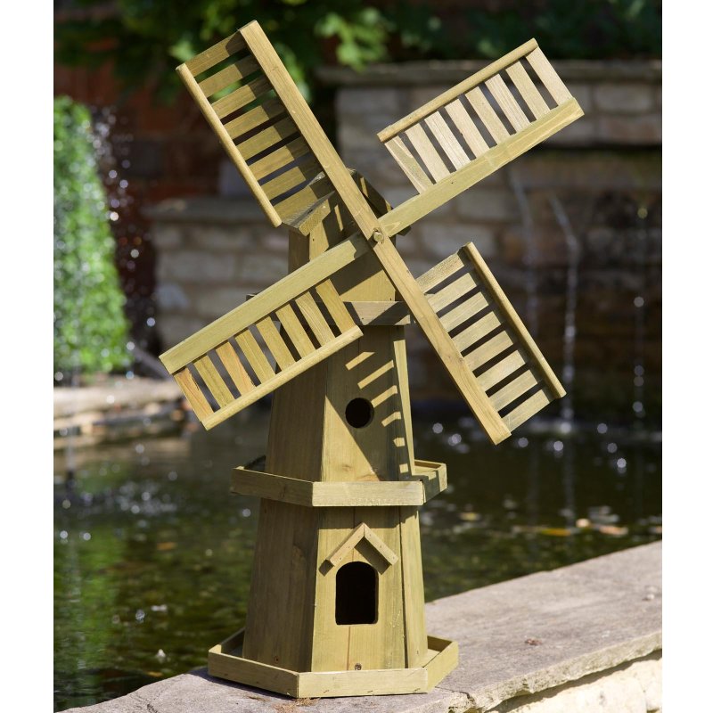 Wooden garden windmill ornament in natural light wood finish with rotating slatted blades, hexagonal base and bird house entrance, positioned beside water feature outdoors