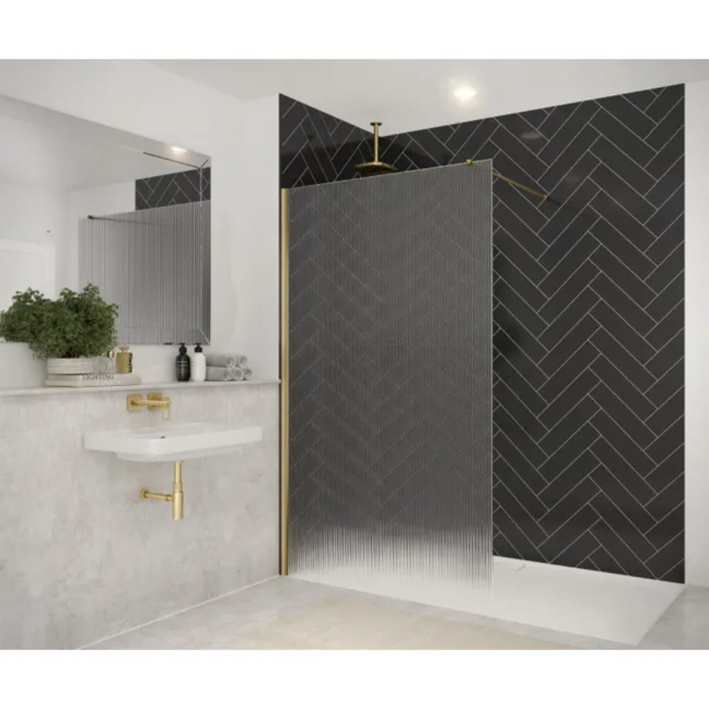 Modern bathroom with Merlyn 8mm wetroom panel featuring textured reeded glass and brushed brass frame, herringbone patterned black tiles on shower wall, white marble-effect tiles, wall-mounted sink with gold fixtures, and contemporary mirror