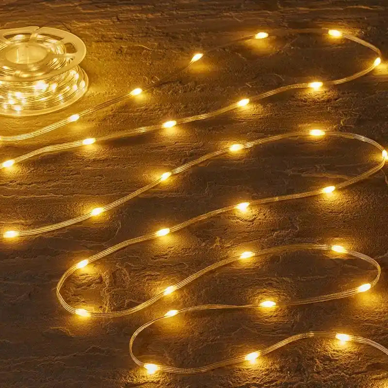Warm white LED string lights coiled on textured brown surface showing illuminated bulbs along clear tubing with controller unit visible in upper left corner