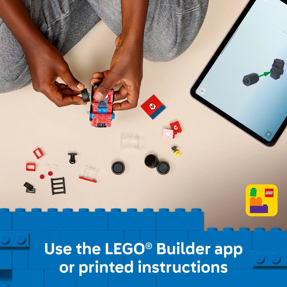 Overhead view of hands assembling a red and blue LEGO fire truck set with various colored bricks and components scattered on a beige surface, alongside a tablet displaying building instructions and the LEGO Builder app logo in the corner