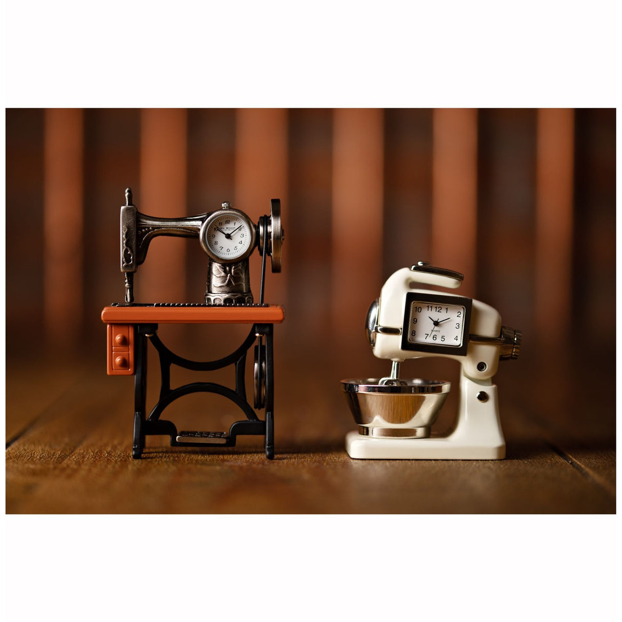 Vintage-style miniature sewing machine clock with cream and chrome metal body featuring an integrated clock face, displayed on a wooden surface against a warm brown striped background, alongside a decorative black and orange treadle sewing machine clock