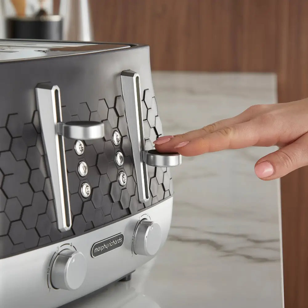Hand inserting bread into a Morphy Richards Cassini 4-slice toaster in moonless night black and white, featuring a hexagonal pattern design and chrome accents on a marble countertop