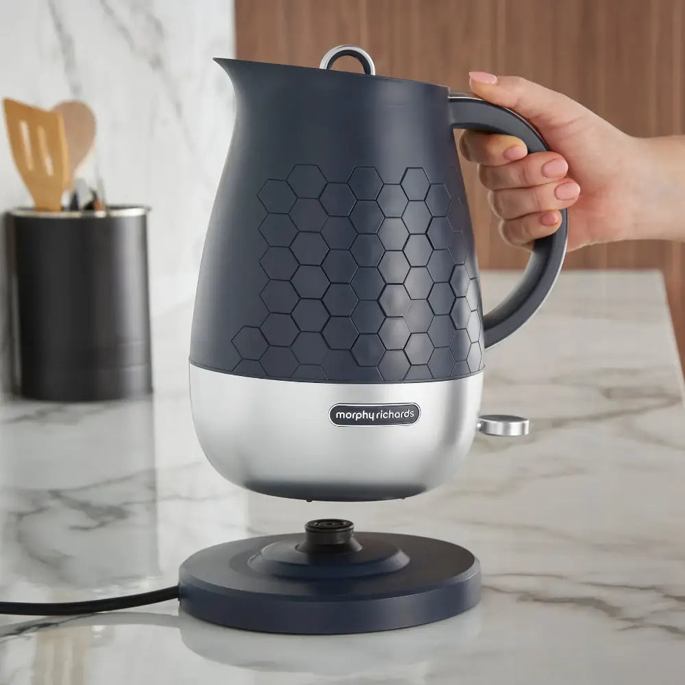 Morphy Richards Cassini 1.7 litre jug kettle in black and silver with honeycomb textured design, held by hand over cordless base on marble countertop in modern kitchen setting
