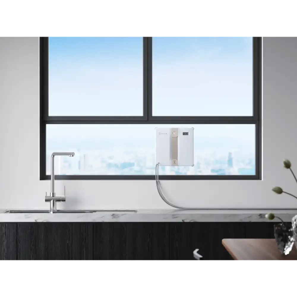 Ecovacs Winbot Mini beige robot window vacuum displayed on a modern kitchen windowsill with stainless steel tap, overlooking a city skyline through black-framed windows