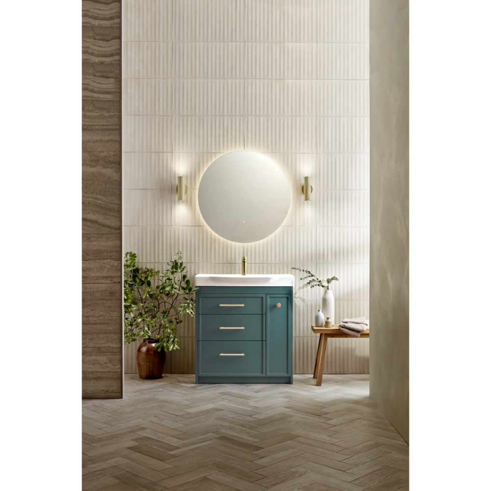 Modern bathroom vanity unit in matt coniston blue with white basin, circular illuminated mirror, brass wall sconces, herringbone wood flooring, vertical tile backsplash, potted plants and wooden accessories