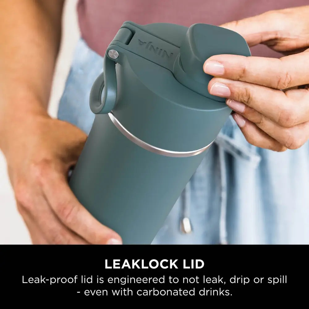 Person holding evergreen insulated Ninja Thirsti 700ml travel bottle displaying the LeakLock lid feature with leak-proof engineering
