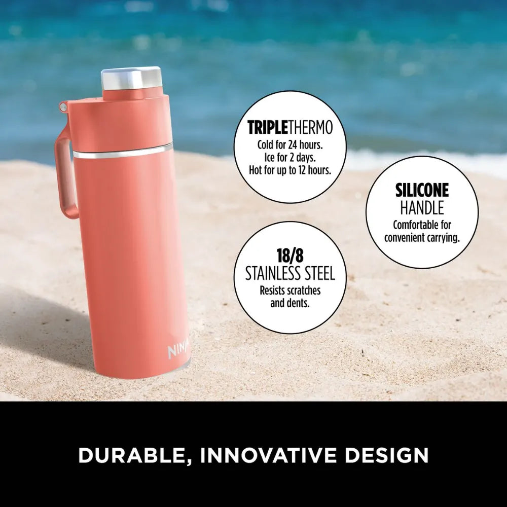 Ninja Thirsti 700ml coral insulated travel bottle on beach sand with ocean background, featuring triple thermo technology, 18/8 stainless steel construction, and silicone handle for carrying